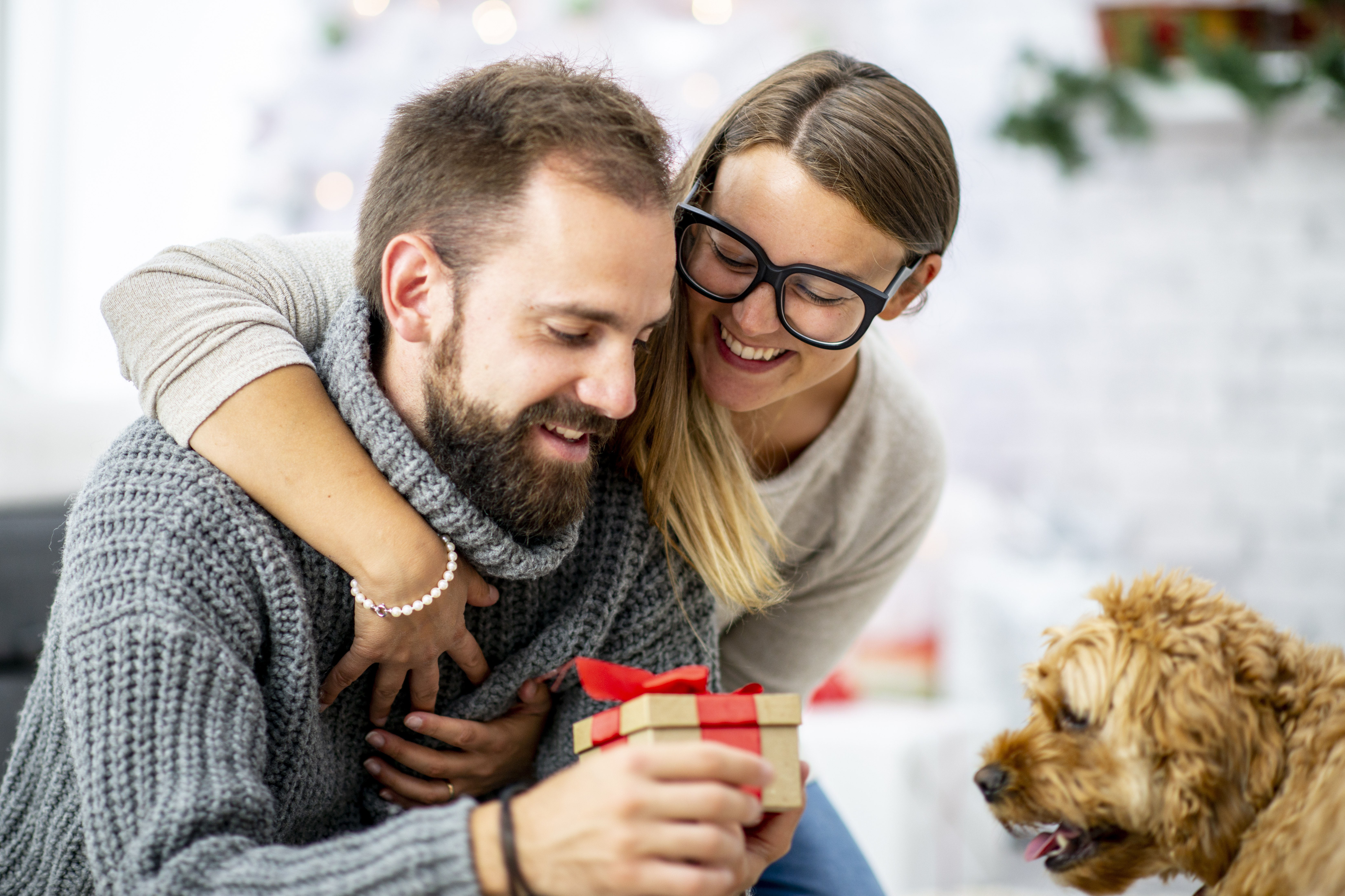 A couple give a gift to their dog on Christmas morning