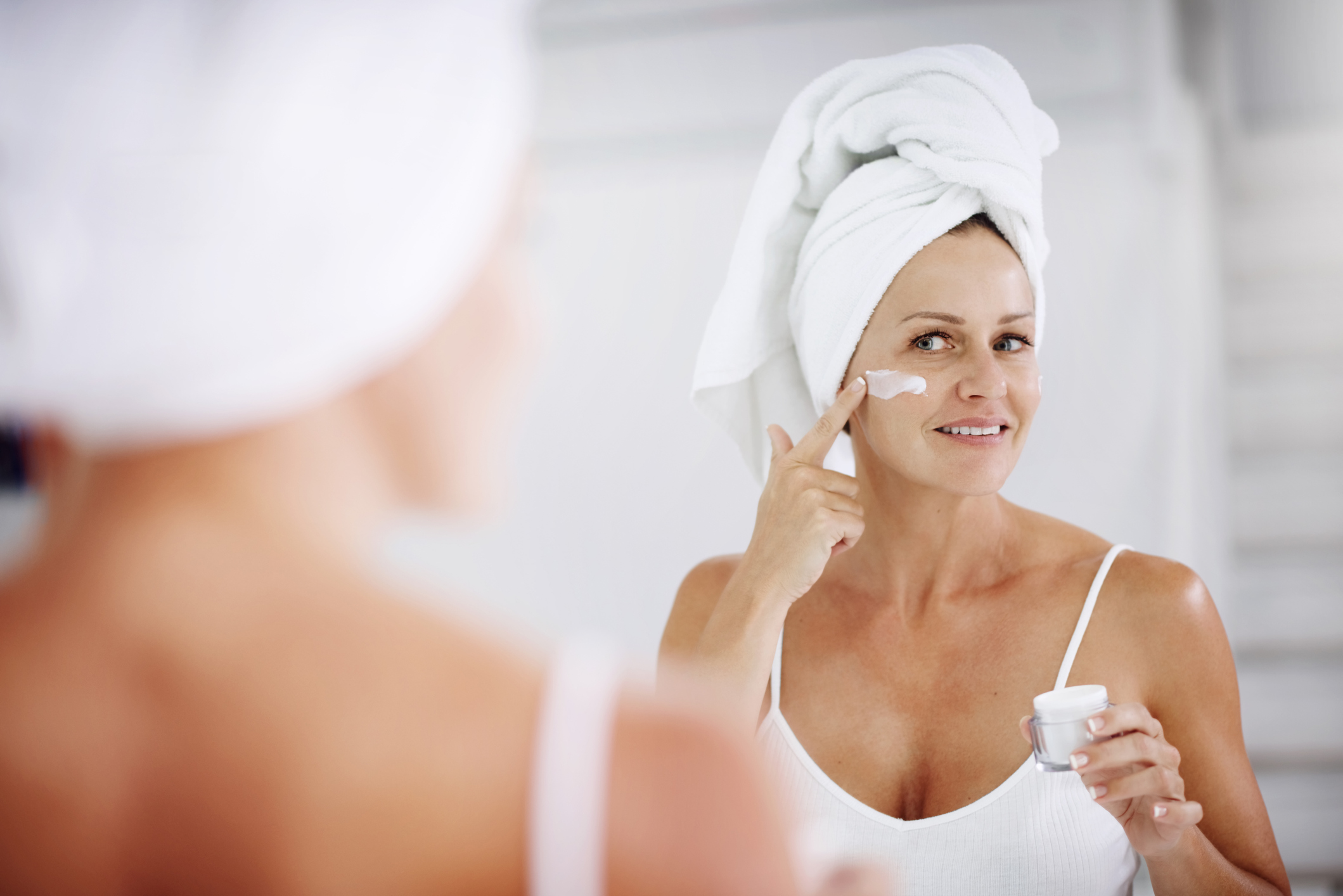 Older woman applies skin cream in the mirror